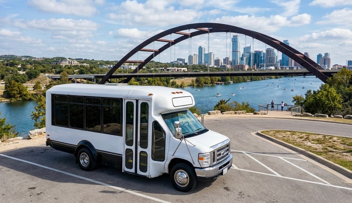 The 16 passenger bus, a white shuttle bus, parked by the water below the Pennybacker Bridge